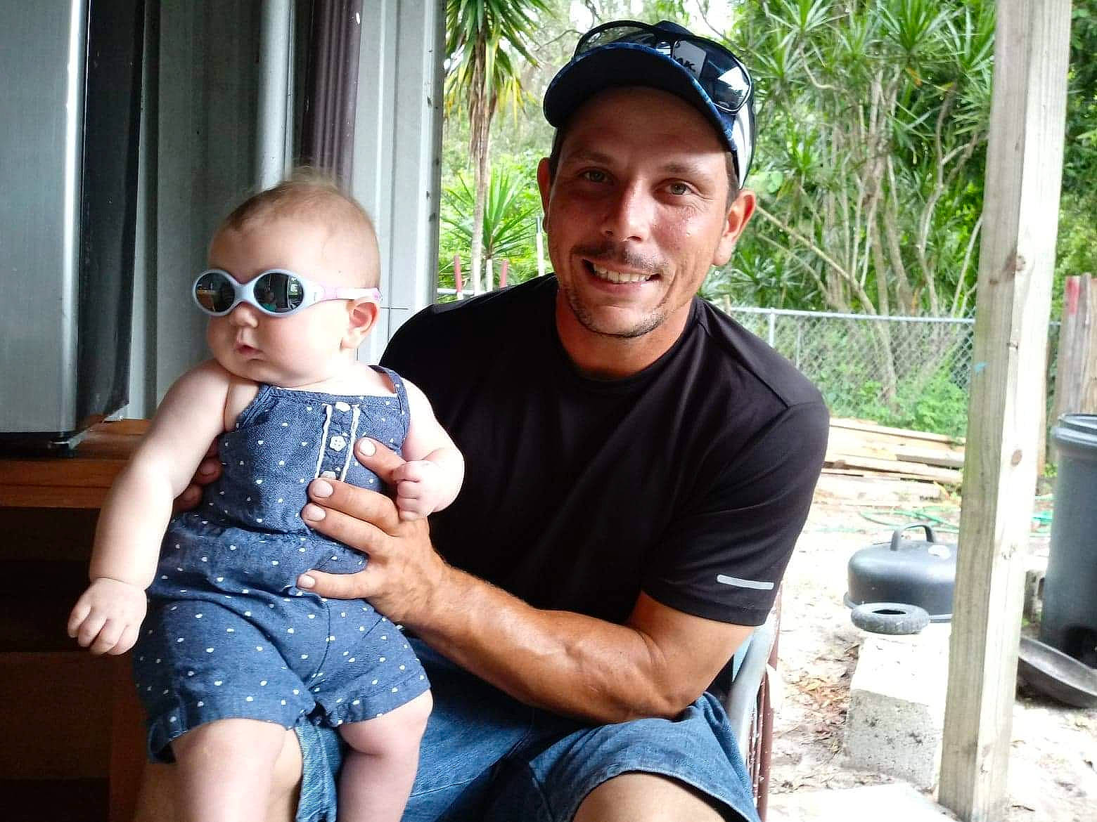 Lilah is registered to the contest to win money with this photo: baby, baby_toddler_clothing, baseball_cap, cap, denim, ear, eyewear, goggles, headwear, human_body, joy, lap, love, mouth, muscle, one_piece_garment, overall, person, sitting, sleeveless_shirt