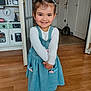child, girl, smiling, indoor, wooden_floor, blue_dress, hair_clips, long_sleeve_shirt, play_kitchen, doorway, home_interior, happy, person, feet, socks, flooring, room, toy_kitchen, young_child, casual_clothing