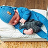 baby, sleeping, blue_outfit, hat, plush_toy, wooden_bed, white_bed, flooring, woven_rug, cozy, infant, child, cute, indoor, resting, soft_toy, knit_fabric, peaceful, portrait, small_bed