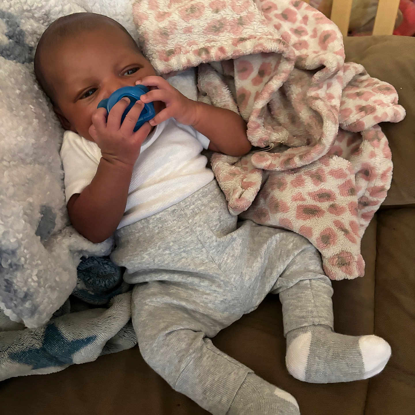 Legend joined the competition — help win amazing prizes! baby, infant, child, portrait, pacifier, smiling, cozy, blanket, pink_blanket, white_blanket, gray_clothing, socks, lying_down, couch, indoor, home, nursery, crib, soft_furnishings, relaxed