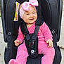 baby, pink_outfit, headband, pink_bow, car_seat, black_car_seat, smiling, infant, child, outdoor, concrete_floor, toy, happy, straps, safety_harness, cute, person, footwear, baby_clothing, playful
