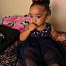 toddler, child, curly_hair, red_bow, blue_dress, stars, bracelet, earrings, bedspread, blanket, mickey_mouse, pink_blanket, indoor, portrait, sitting, cute, thoughtful, hand_on_mouth, young_child, cozy