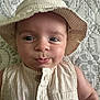 baby, child, hat, bucket_hat, striped_clothing, beige, close_up, portrait, cute, infant, pout, face, blue_eyes, sleeveless, buttoned_shirt, quilt, patterned_background, skin, person, lying_down