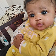Keymeira is registered to the contest to win money with this photo: baby, infant, child, portrait, close_up, wide_eyes, curly_hair, yellow_outfit, hearts, smiling, indoor, crib, nursery, blanket, plush_toy, seated, cozy, lifestyle, photography, adorable