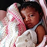 Koi is registered to the contest to win money with this photo: baby, infant, child, portrait, face, eyes, looking_at_camera, curly_hair, blanket, crochet, pastel_colors, pink, white, blue, stroller, cozy, seated, indoors, close_up, adorable