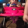 baby, child, toy_car, walker, indoor, legs, face, curious, red, plastic, playtime, furniture, floor, shadow, arm, person, seat, head, expression, home