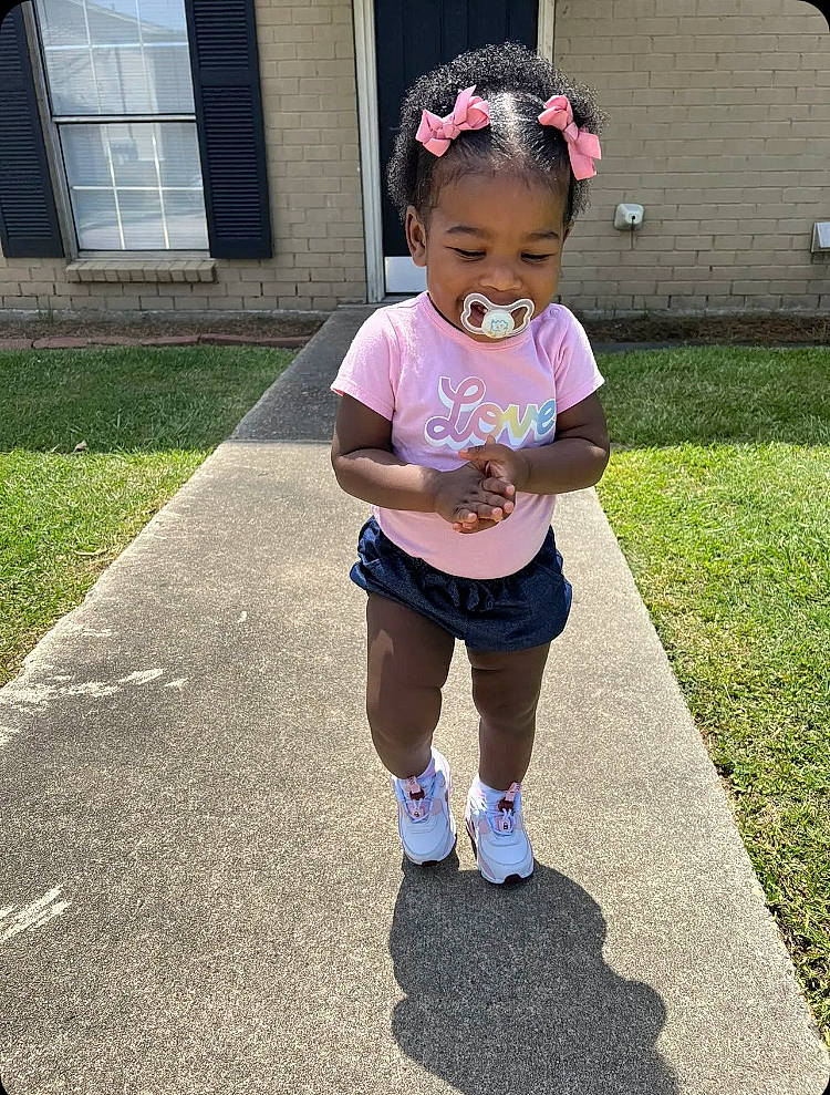 Gianna is registered to the contest to win money with this photo: asphalt, baby, baby_toddler_clothing, cap, eyewear, grass, happy, hat, human_leg, knee, leisure, person, pink, recreation, shorts, sidewalk, sleeve, t_shirt, thigh, toddler