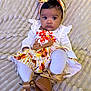 baby, infant, child, headband, bow, white_clothing, patterned_skirt, boots, blanket, texture, laying_down, cute, portrait, indoors, young_child, looking_at_camera, fall_colors, ribbons, small_feet, cozy