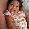Elizabeth is registered to the contest to win money with this photo: baby, smiling, tongue_out, bracelet, floral_outfit, pink_cushion, cute, lying_down, infant, person, happy, child, soft_texture, indoors, portrait, cute_expression, hand, face, hair, skin