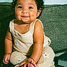 Elizabeth is registered to the contest to win money with this photo: baby, child, smiling, curly_hair, knit_outfit, flower_pattern, sitting, couch, indoor, cute, happy, portrait, infant, small_hands, bare_feet, dark_hair, cozy, comfortable, home, adorable