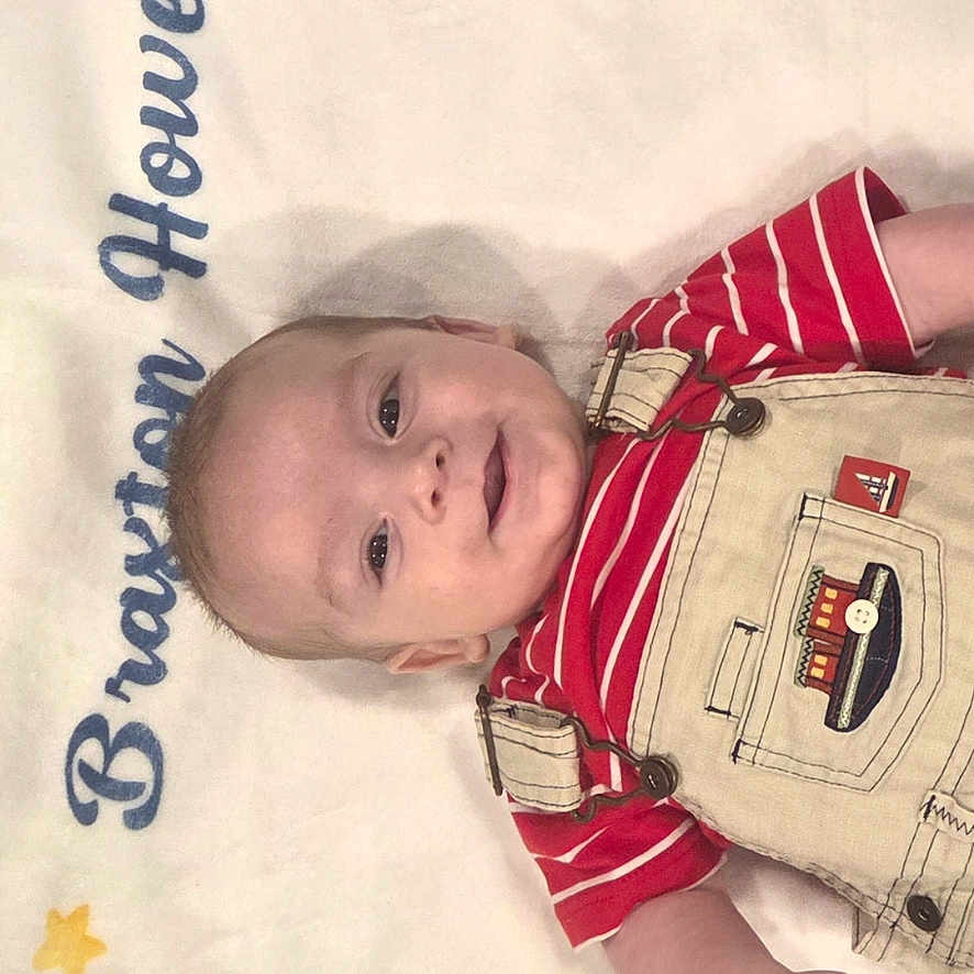 Braxton is registered to the contest to win money with this photo: baby, infant, smiling, overalls, red_shirt, blanket, stars, clouds, face, person, child, cute, portrait, lying_down, happy, indoor, young_child, clothing, baby_boy, soft_texture