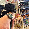 puppy, dog, black_dog, person, hand, watch, store, snacks, shelves, shopping, aisle, food, retail, holding, cute, pet, indoor, furniture, resting, white_markings