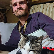 Queen Mini is registered to the contest to win money with this photo: animal, beard, casual, cat, comfort, couch, cozy, curtains, feline, game_controller, home, indoor, lanyard, man, nap, pet, portrait, purple_shirt, red, relaxed