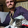 animal, beard, casual, cat, comfort, couch, cozy, curtains, feline, game_controller, home, indoor, lanyard, man, nap, pet, portrait, purple_shirt, red, relaxed