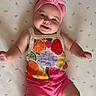 baby, infant, smiling, headband, flower, pink, fruit_pattern, clothing, lying_down, blanket, cute, happy, child, portrait, skin, arm, leg, indoors, baby_girl, colorful
