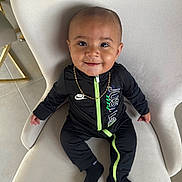 Kencio participe au concours pour gagner de l'argent avec cette photo : baby, child, smiling, black_clothing, nike, gold_chain, chair, indoor, portrait, cute, sitting, black_socks, floor, tile_floor, happy, young_child, fashion, person, head, face