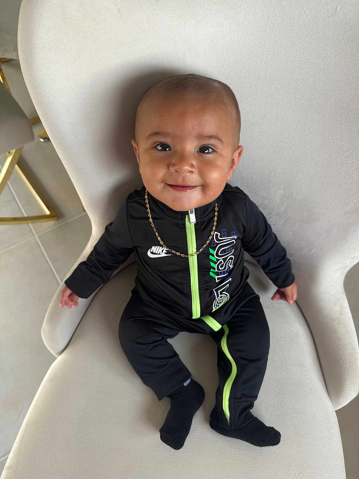 Kencio participe au concours pour gagner de l'argent avec cette photo : baby, child, smiling, black_clothing, nike, gold_chain, chair, indoor, portrait, cute, sitting, black_socks, floor, tile_floor, happy, young_child, fashion, person, head, face