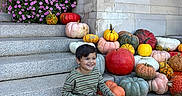 Caden joined the competition — help win amazing prizes! child, boy, smiling, sitting, outdoor, steps, pumpkins, gourds, autumn, fall, flowers, pink_flowers, brick_building, stone_steps, portrait, striped_shirt, pants, sneakers, house_entrance, daylight