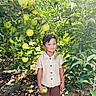 Caden is registered to the contest to win money with this photo: child, boy, apple_tree, apples, orchard, outdoor, nature, garden, fruit, greenery, leaves, portrait, standing, smiling, sunlight, summer, shorts, shirt, holding_fruit, rustic