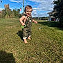 toddler, child, grass, outdoor, sunny, sky, clouds, overalls, barefoot, toy, american_flag, power_lines, building, greenery, happy, smiling, nature, daylight, person, playing