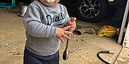 Kolter is registered to the contest to win money with this photo: bag_of_material, child, concrete_floor, garage, grey_sweatshirt, hair_messy, hose, indoor, muddy_pants, pacifier, person, standing, toddler, tool, toy_in_background, truck, white_shoes, work_boots, wrench, young_child
