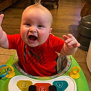 Hagen joined the competition — help win amazing prizes! baby, child, walker, toy, piano_keys, smiling, happy, indoor, living_room, floor, furniture, television, red_shirt, hair, hands, seat, playtime, cute, infant, home