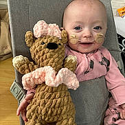 Clara is registered to the contest to win money with this photo: baby, child, smiling, indoor, toy, teddy_bear, knitted_toy, pink_clothing, nasal_tube, medical, seat, fabric, cute, infant, happy, person, plush, soft_toy, holding, cozy