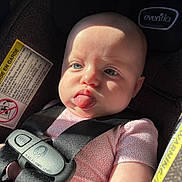 Charlotte is registered to the contest to win money with this photo: baby, infant, car_seat, child, safety_harness, tongue_out, blue_eyes, close_up, cute, sunlight, seatbelt, pink_clothing, head, face, expression, straps, car_interior, child_safety, person, portrait