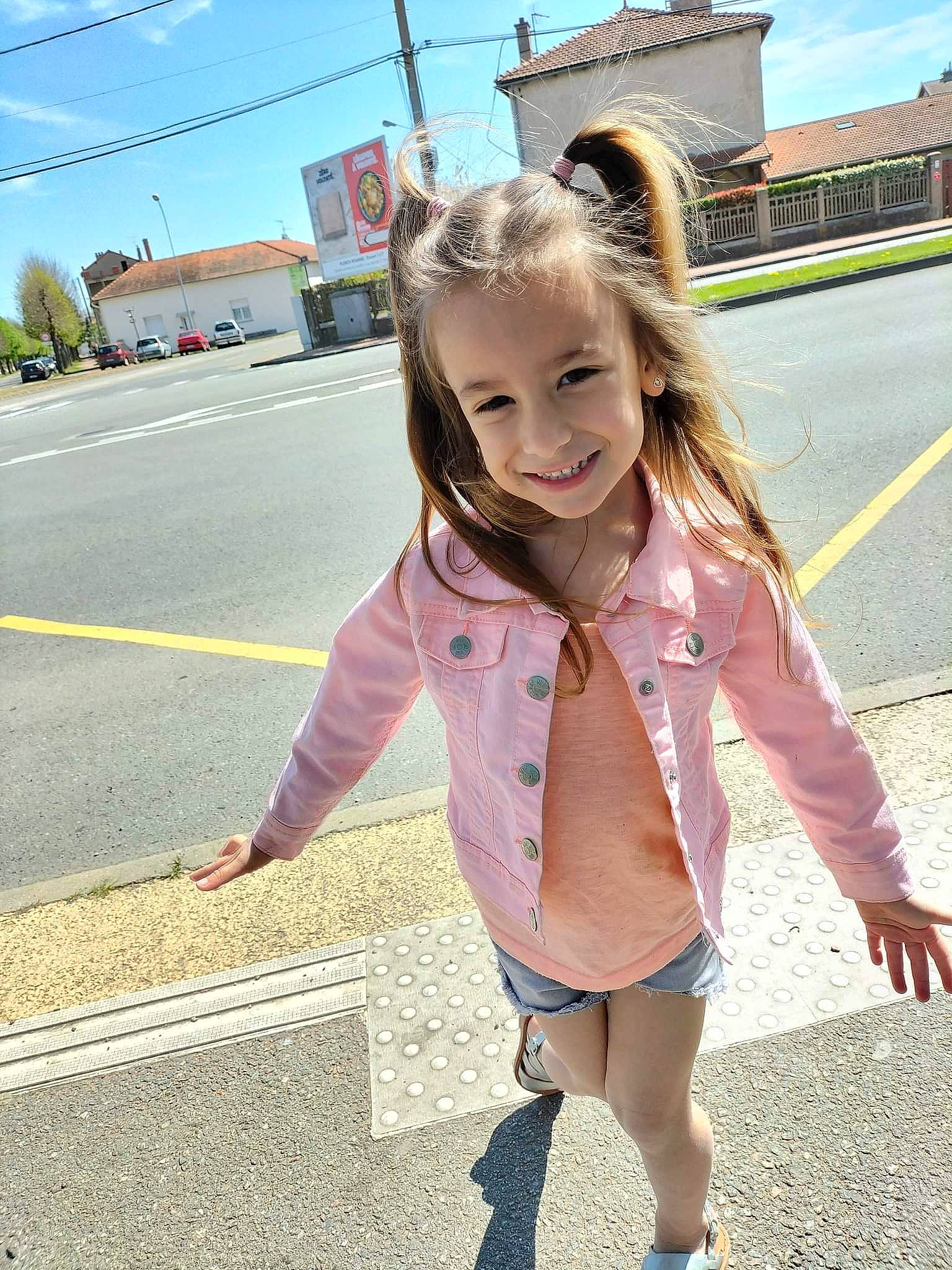 Maëlya participe au concours pour gagner de l'argent avec cette photo : asphalt, blond, cool, denim, electric_blue, facial_expression, fun, hairstyle, happy, joy, long_hair, outerwear, person, pink, road_surface, sky, sleeve, smile, thigh, toddler