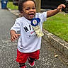 toddler, child, smiling, happy, birthday, ribbon, dollar_bill, nike, soccer, red_shorts, sneakers, outdoor, street, sidewalk, greenery, car, celebration, walking, person, joyful
