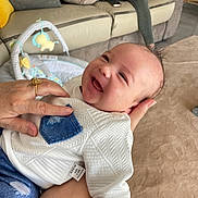 Marius participe au concours pour gagner de l'argent avec cette photo : baby, blanket, blue_jeans, child, clothing, couch, cushion, denim, face, floor, hand, happy, holding, indoor, living_room, person, portrait, smiling, toy, white_shirt
