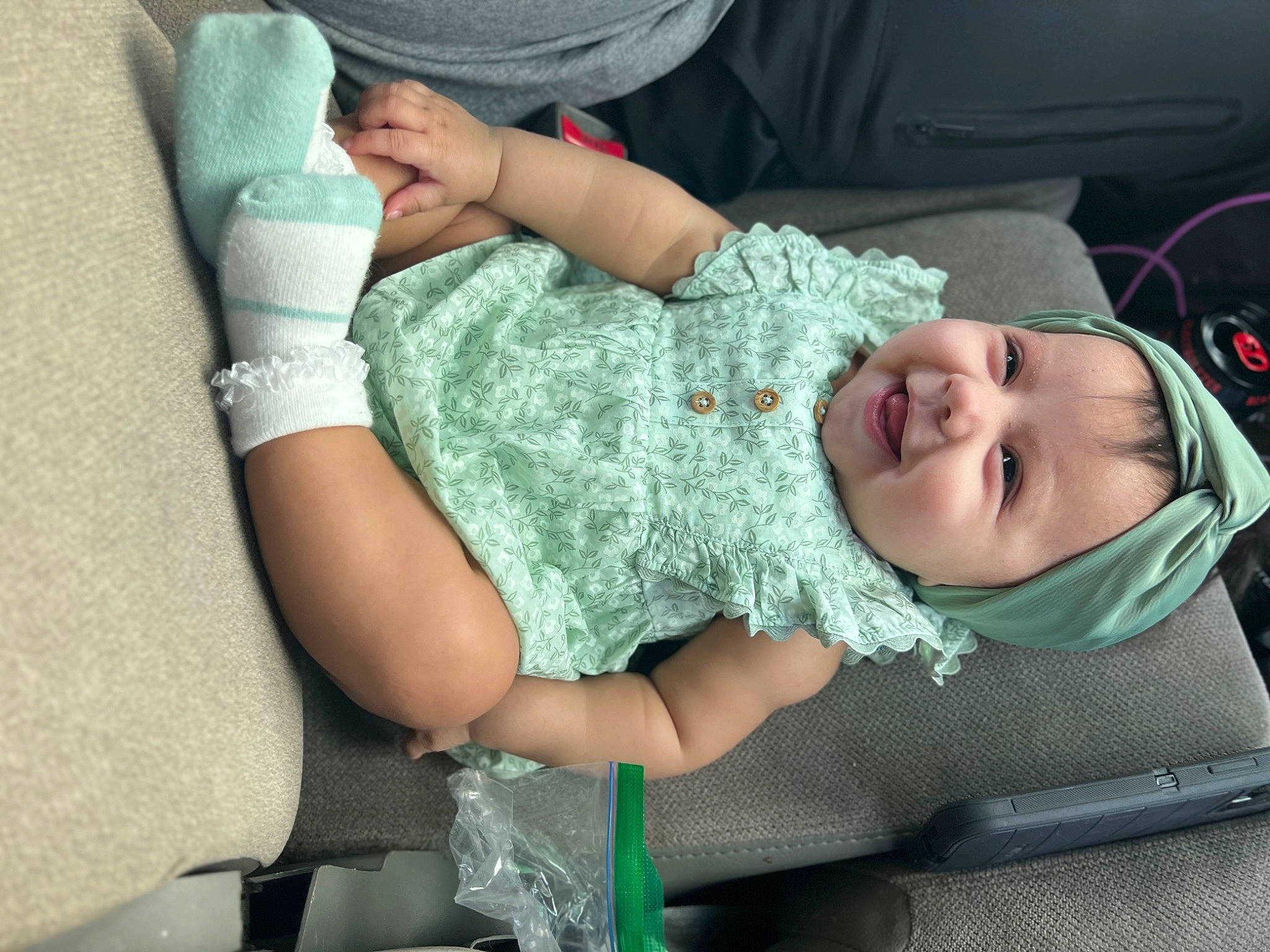 Aiyana is registered to the contest to win money with this photo: baby, baby_products, baby_toddler_clothing, child, comfort, elbow, gesture, happy, hat, headwear, human_leg, joy, lap, linens, nail, pattern, person, sitting, sleeve, smile