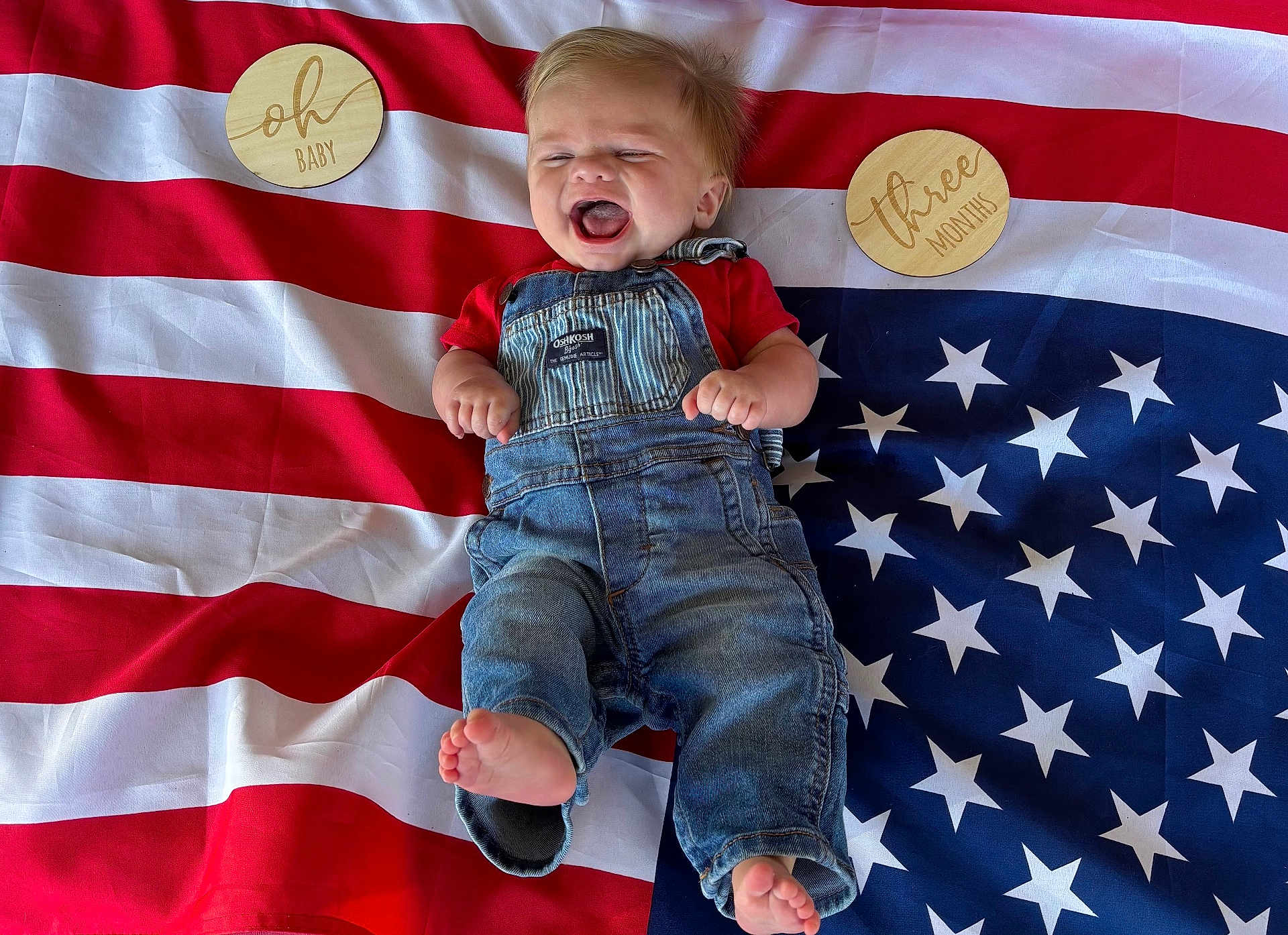 Grant joined the competition — help win amazing prizes! baby, infant, denim_overalls, red_shirt, american_flag, stars, stripes, wooden_plaques, milestone, three_months, oh_baby, happy, laughing, barefoot, lying_down, celebration, cute, child, portrait, clothing
