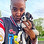 Oreo joined the competition — help win amazing prizes! person, dog, puppy, outdoor, trees, sky, jacket, hand, face, animal, cute, affection, grass, park, young_adult, smile, holding, casual, expression, nature