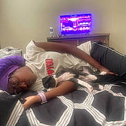 Oreo joined the competition — help win amazing prizes! person, sleeping, dog, puppy, bed, blanket, glasses, headwrap, black_and_white, arm, indoor, television, screen, furniture, casual_clothing, rest, cozy, nap, relaxation, couch