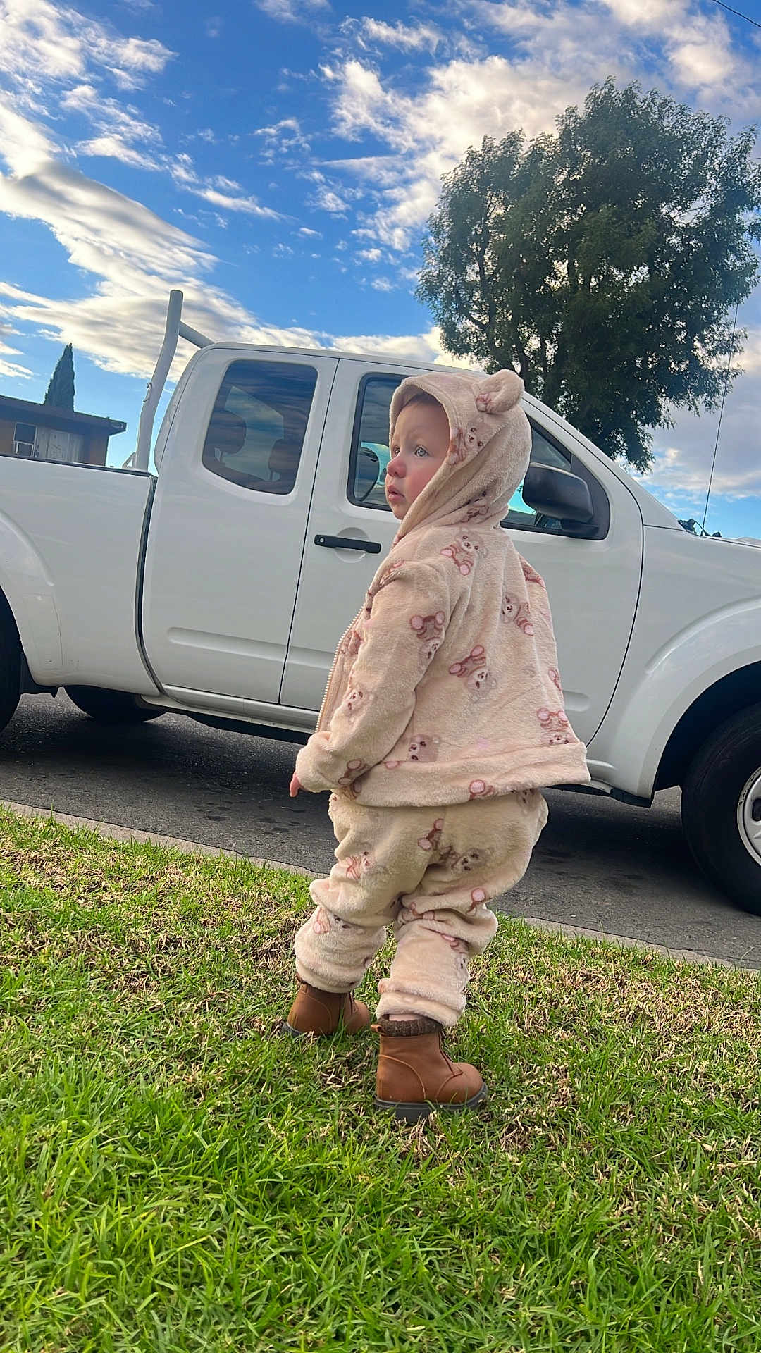 Suzie is registered to the contest to win money with this photo: toddler, child, grass, outdoor, clouds, sky, tree, truck, vehicle, boots, hoodie, cute, warm_clothing, side_view, daylight, curious, casual, nature, street, young_child