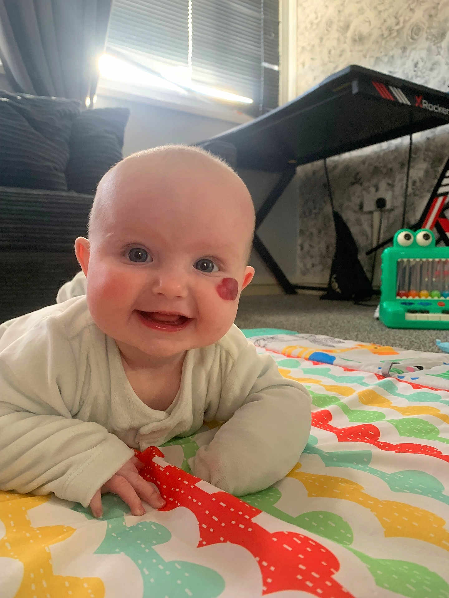 Daisy joined the competition — help win amazing prizes! baby, infant, smiling, face, birthmark, play_mat, indoor, toy, couch, keyboard_stand, carpet, child, happy, clothing, person, cute, expression, floor, home, colorful