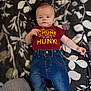 baby, infant, clothing, jeans, tshirt, lying_down, blanket, pattern, floral, person, cute, child, casual, indoor, blue_jeans, maroon_shirt, small_child, young_baby, apparel, relaxed