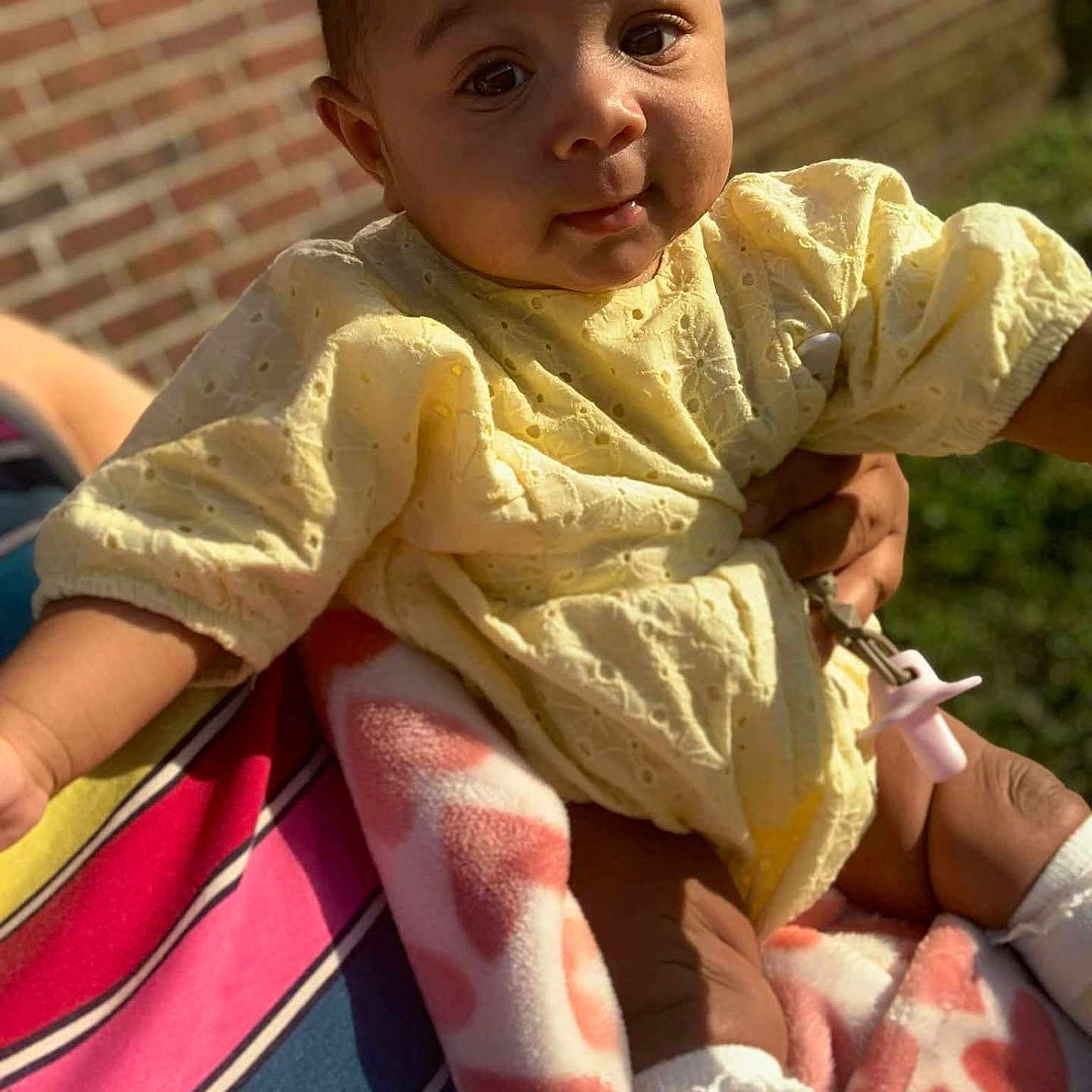 Jae'Onti joined the competition — help win amazing prizes! baby, child, infant, yellow_clothing, blanket, striped_shirt, brick_wall, outdoor, sunlight, person, holding, cute, face, portrait, hand, sock, toddler, smiling, skin, fabric