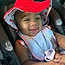 Jae'Onti joined the competition — help win amazing prizes! baby, child, car_seat, red_hat, pacifier, smiling, happy, infant, bib, seatbelt, car_interior, cute, young, person, clothing, safety, headwear, portrait, closeup, hand