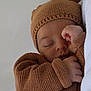 baby, sleeping, knitted_hat, knitted_sweater, cozy, infant, peaceful, closed_eyes, cute, warm, newborn, soft_texture, resting, small_hands, portrait, child, indoors, relaxed, headwear, blanket