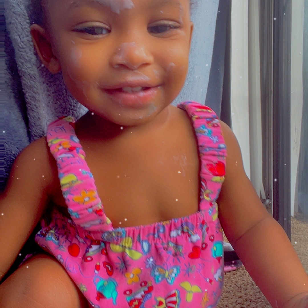 Marziyah is registered to the contest to win money with this photo: carpet, child, colorful_beads, cute, face, hair_accessories, happy, indoor, natural_light, patterned_clothing, person, pink_outfit, playful, portrait, sitting, skin, smiling, toddler, window, young_child