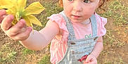 Riley joined the competition — help win amazing prizes! child, toddler, curly_hair, red_hair, flower, overalls, pink_shirt, outdoors, grass, dirt, boots, portrait, hand, offering, blue_eyes, cute, candid, sunlight, playful, nature