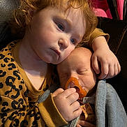 Riley joined the competition — help win amazing prizes! child, toddler, baby, sibling, pacifier, blanket, cuddling, curly_hair, sleeping, indoor, portrait, closeup, hands, cozy, leopard_print, sweater, soft_lighting, toy_wheel, sofa, affection