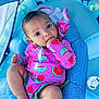 baby, infant, child, watermelon_pattern, colorful_clothing, sitting, pacifier, blue_cushion, hand_in_mouth, indoor, cute, portrait, soft_lighting, comfortable, close_up, young_child, child_fashion, baby_gesture, fabric_pattern, relaxing