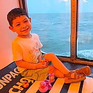 Ace joined the competition — help win amazing prizes! child, boy, smiling, sitting, window, sea, water, toy, rubber_duck, sandals, shorts, tshirt, indoor, playtime, happy, casual_clothing, legs_crossed, daylight, reflection, relaxation