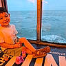 Ace is registered to the contest to win money with this photo: child, boy, smiling, toy, rubber_duck, window, ocean, boat, indoor, casual_clothing, shorts, tshirt, footwear, sandals, seascape, water, playful, happy, sitting, travel