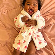 Amaia is registered to the contest to win money with this photo: baby, child, smiling, robe, blanket, happy, cute, infant, cozy, pink, pattern, lying_down, portrait, young_child, indoor, soft_texture, hands, legs, face, expression