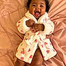 baby, blanket, child, cozy, cute, expression, face, hands, happy, indoor, infant, legs, lying_down, pattern, pink, portrait, robe, smiling, soft_texture, young_child