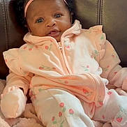 Naiari is registered to the contest to win money with this photo: baby, infant, pink_clothing, headband, flower, couch, blanket, soft_texture, curly_hair, cute, portrait, child, indoor, cozy, sitting, comfort, young_child, looking_at_camera, small_hands, adorable